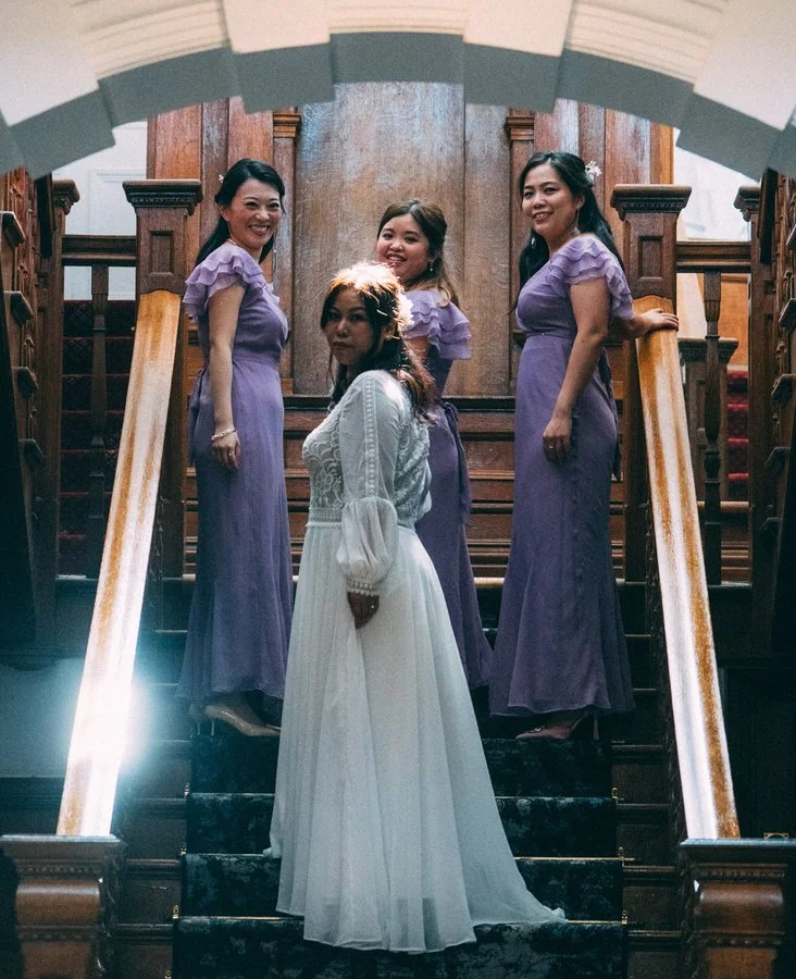 Bridesmaids in lilac dresses gathered on a grand staircase with the bride